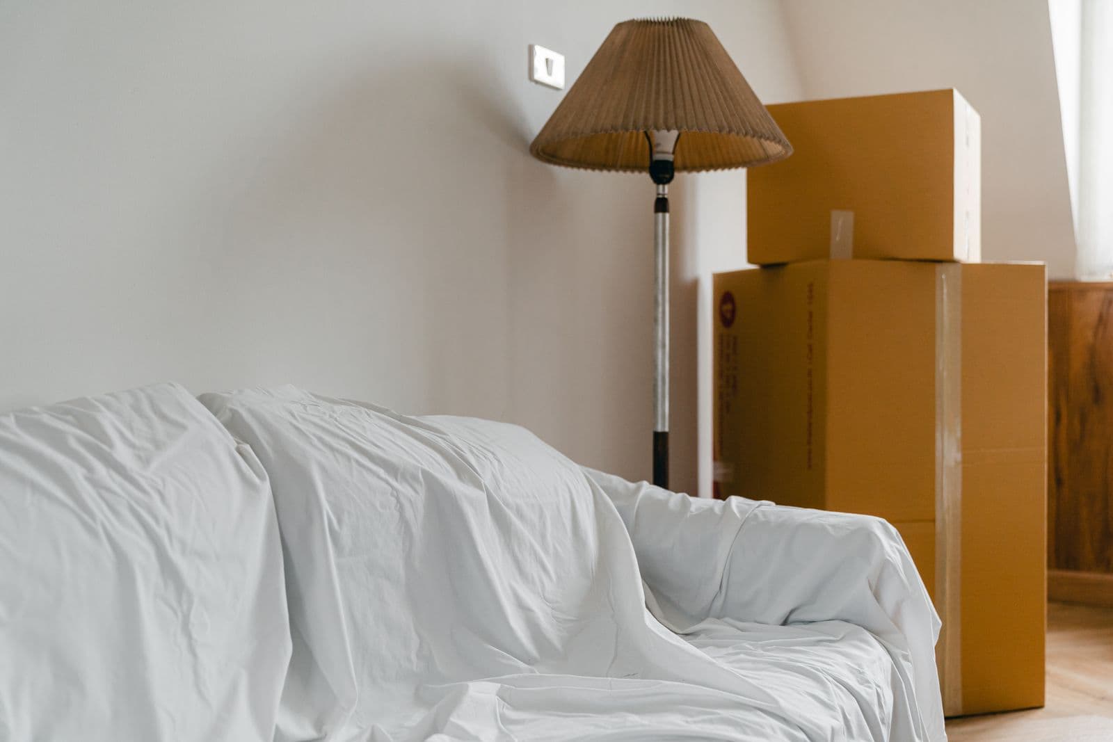 Canapé protégé d'un drap et cartons de déménagement dans une pièce vide