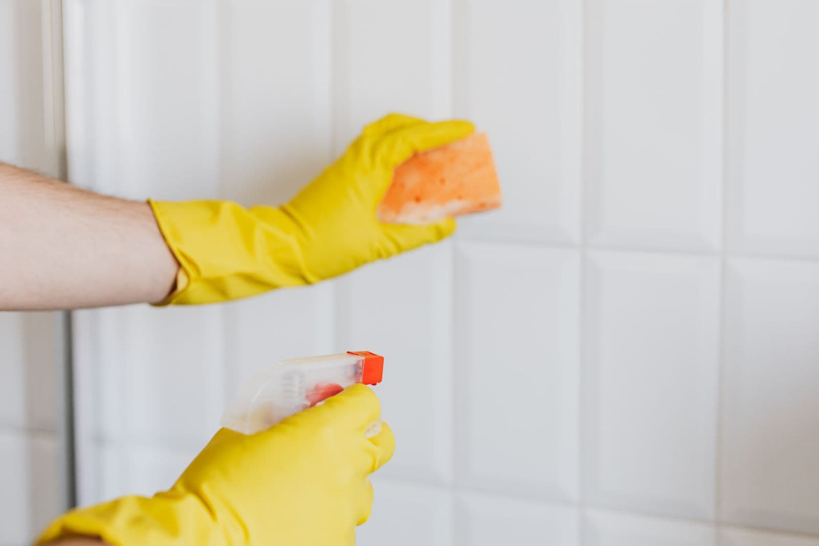 Mains gantées nettoyant une faïence blanche à l'éponge